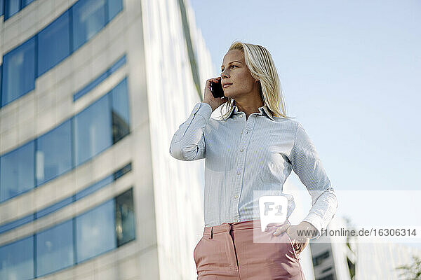 Blonde Geschäftsfrau  die mit ihrem Smartphone telefoniert und dabei auf das Finanzviertel blickt