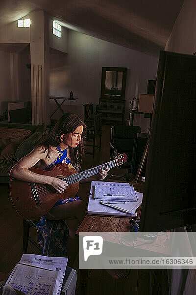 Junge Frau übt Gitarre im Wohnzimmer zu Hause