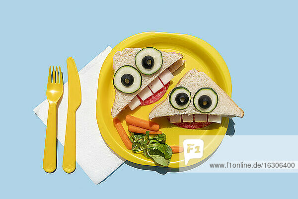 Studioaufnahme eines Plastiktellers mit zwei lustig aussehenden Sandwiches mit anthropomorphen Gesichtern