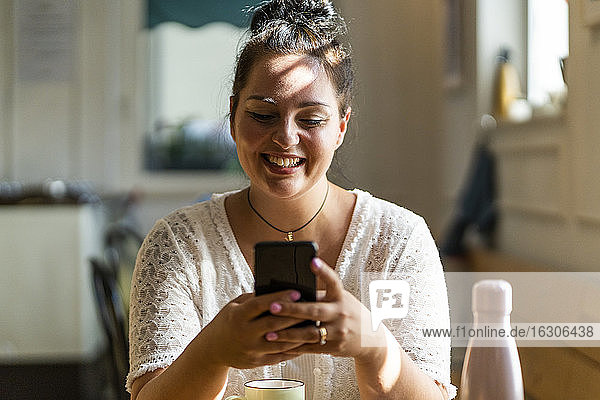Nahaufnahme einer lächelnden  üppigen Frau  die ein Mobiltelefon benutzt  während sie im Restaurant sitzt