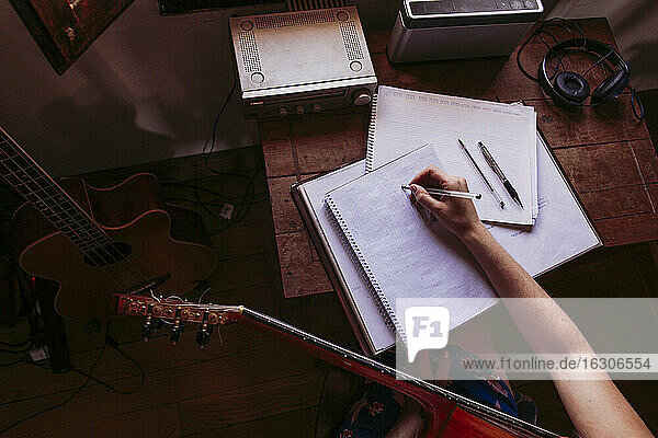 Junge Frau schreibt in ein Buch  während sie zu Hause Gitarre übt