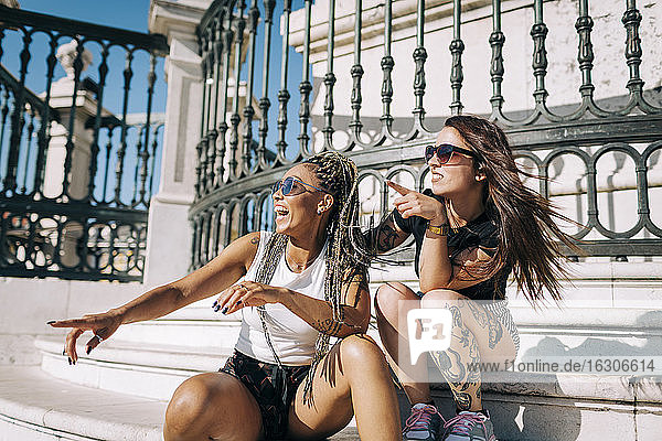Female friends laughing while pointing against fence at Praca Do Comercio  Lisbon  Portugal