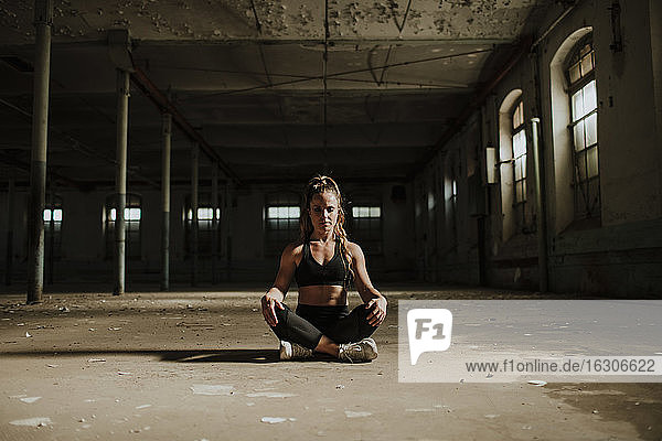 Sportler meditiert sitzend in einer verlassenen Fabrik