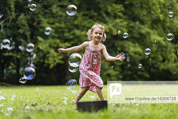Lächelndes Mädchen läuft inmitten von Seifenblasen im Park