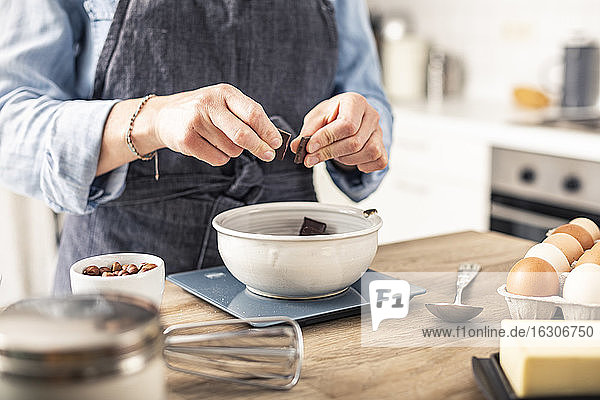 Frau wiegt Schokolade auf einer Küchenwaage  während sie zu Hause an der Kücheninsel steht