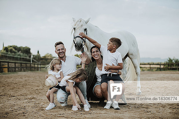 Cheerful parents with children crouching by horse in barn