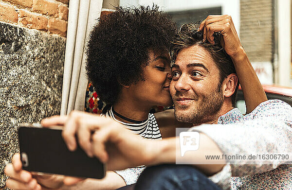 Nahaufnahme einer romantischen Freundin  die ihren Freund küsst  der ein Selfie mit ihr im Café macht