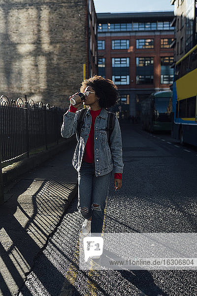 Junge Frau trinkt Kaffee beim Spaziergang auf der Straße in der Stadt