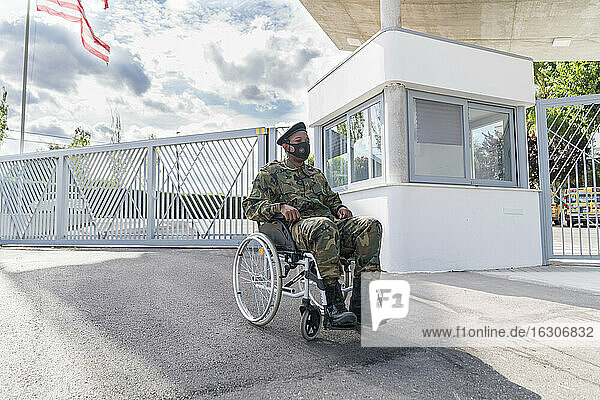 Armeesoldat mit Gesichtsschutzmaske im Rollstuhl sitzend vor bewölktem Himmel