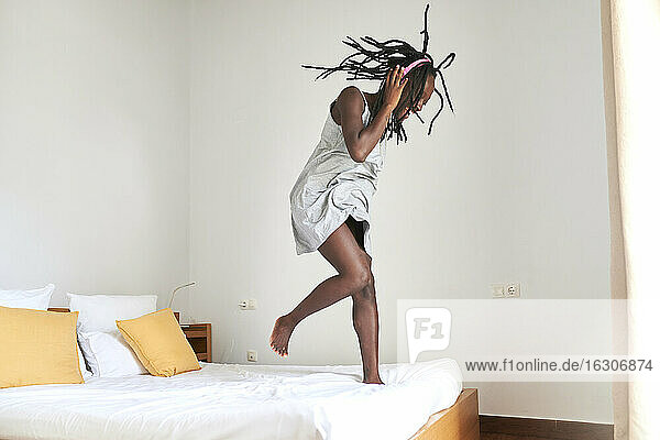 Junge Frau beim Tanzen und Musikhören auf dem Bett zu Hause