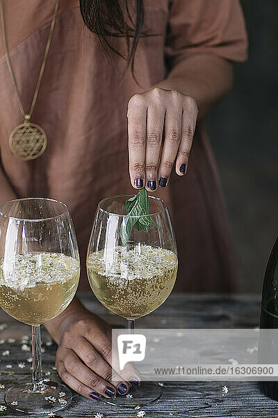 Mittelteil einer Frau  die bei der Zubereitung eines Cocktails Minzblätter über ein Weinglas hält