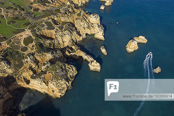 Portugal  Algarve  Lagos  Drohnenansicht eines Motorboots  das an den Schornsteinen der Landzunge Ponta da Piedade vorbeifährt
