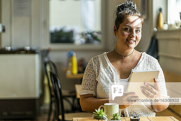 Lächelnde üppige Frau  die ein digitales Tablet benutzt  während sie in einem Café sitzt