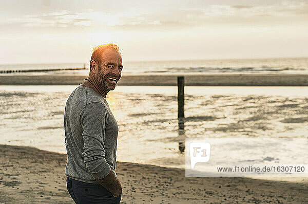 Cheerful mature man standing against sea during sunset at weekend