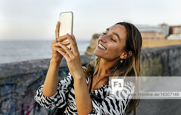 Lächelnde junge Frau beim Fotografieren auf der Promenade