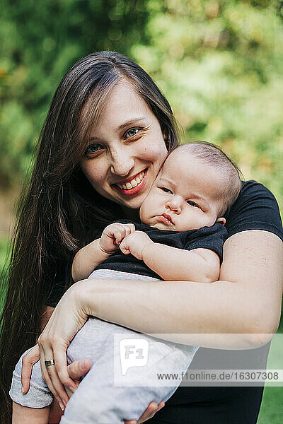 Smiling young woman carrying baby boy at park