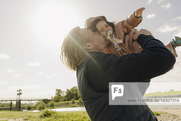 Vater küsst Baby Tochter auf die Wange in der Nähe Flussufer am sonnigen Tag