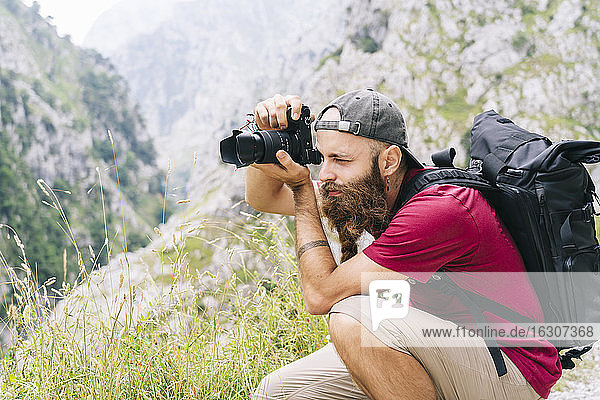 Young man taking photo through camera while sitting on mountain at Ruta Del Cares  Asturias  Spain