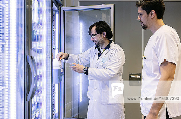Male pharmacists taking inventory from illuminated refrigerator in hospital