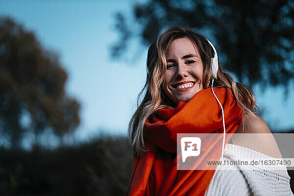 Lächelnde junge Frau  die bei Sonnenuntergang im Wald Musik hört