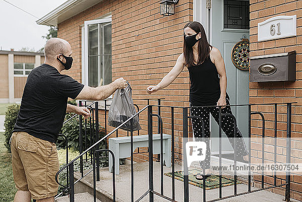 Woman taking plastic bag from delivery man with protective mask