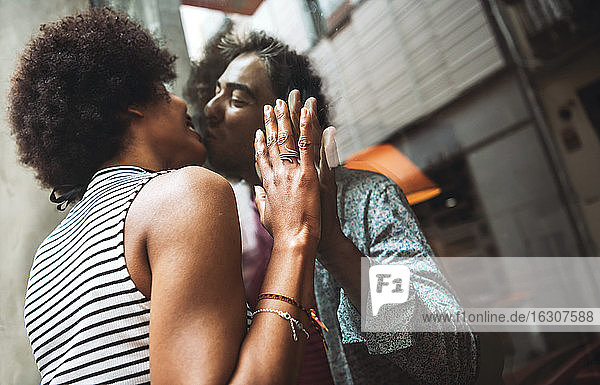 Romantische Frau  die ihren Freund durch das Fenster eines Cafés küsst  während sie im Freien steht