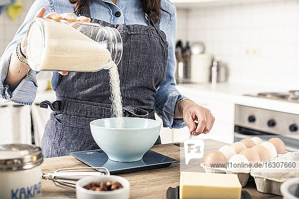 Frau wiegt Mehl auf einer Küchenwaage für die Zubereitung von Kuchen zu Hause
