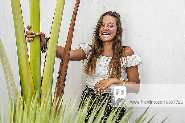 Lächelnde Frau  die eine Pflanze hält und an der Wand steht