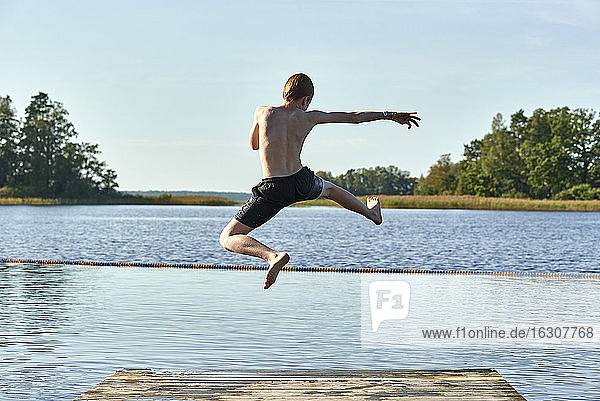 Rothaariger Junge springt in den See gegen den klaren Himmel