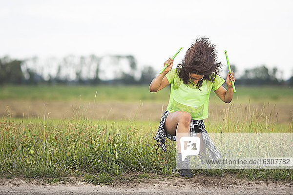 Junge Frau mit zerzaustem Haar  die auf einem Feld die Trommelstöcke hält