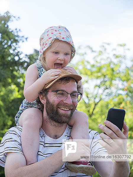 Daughter sticking out tongue while father taking selfie on smart phone