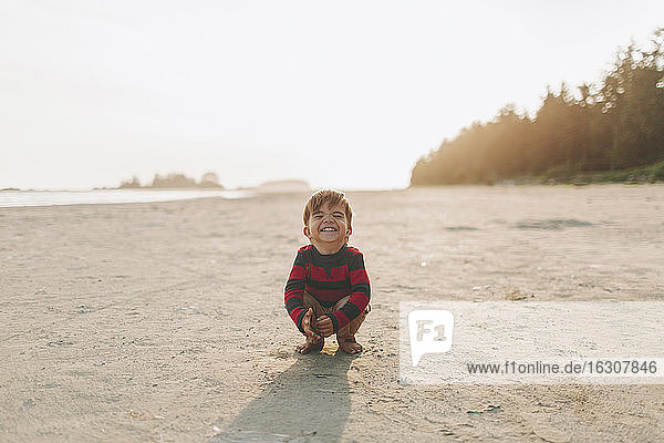 Niedlicher Junge hockt beim Spielen im Sand am Strand