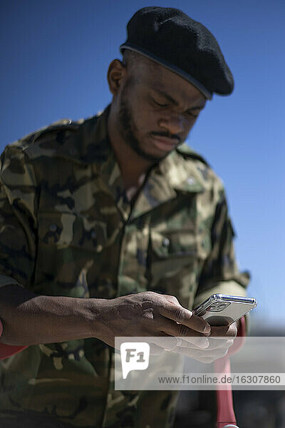 Militäroffizier mit Krücken  der an einem sonnigen Tag eine Textnachricht auf seinem Smartphone schreibt