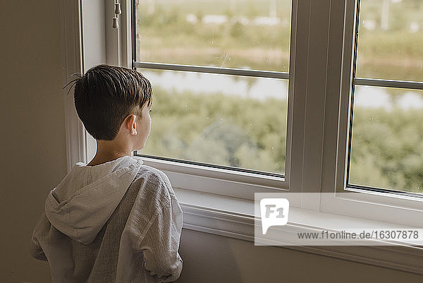 Junge schaut durch das Fenster  während er zu Hause steht