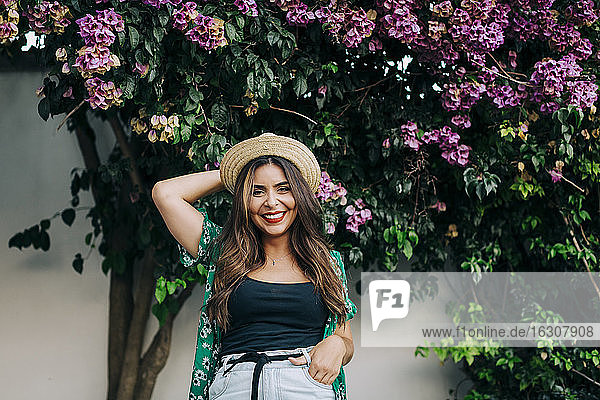 Fröhliche junge Frau mit Hut vor Pflanzen stehend