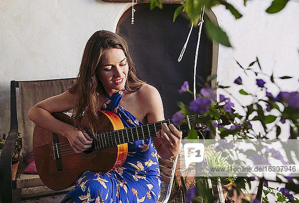 Junge Frau spielt Gitarre  während sie auf dem Balkon sitzt