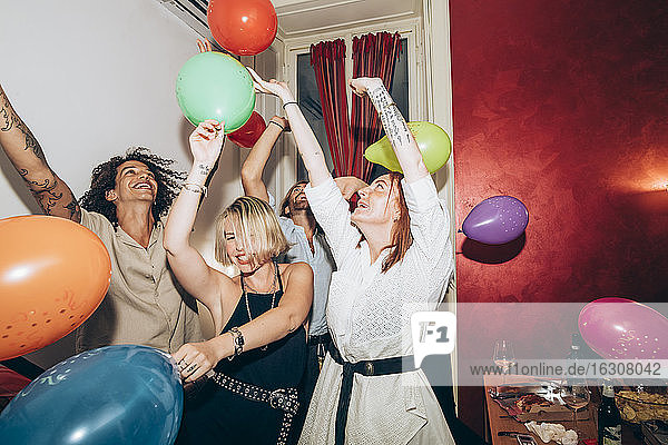 Männliche und weibliche Freunde tanzen mit bunten Luftballons während einer Party