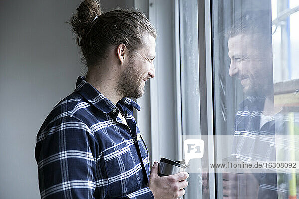 Bauarbeiter  der einen Container hält und durch das Fenster seines Hauses schaut