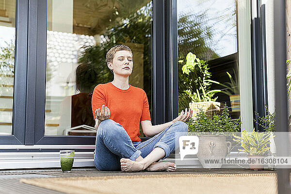 Mittlere erwachsene Frau meditiert  während sie auf einer Veranda gegen das Haus sitzt
