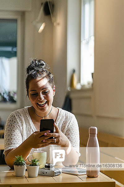 Fröhliche junge Frau  die ein Mobiltelefon benutzt  während sie am Tisch im Restaurant sitzt