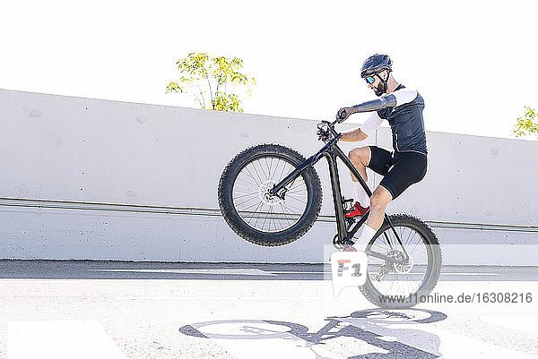 Männlicher Sportler mit Beinprothese bei einem Stunt mit dem Fahrrad auf der Straße gegen den klaren Himmel