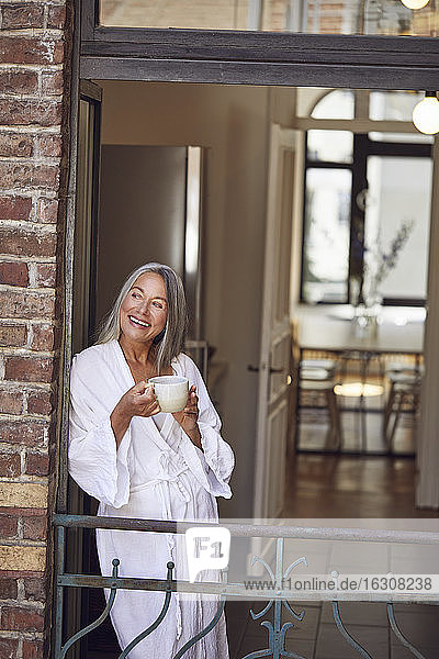 Glückliche Frau trinkt Tee auf dem Balkon