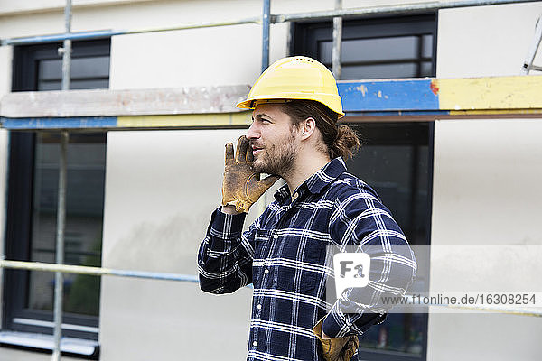 Bauarbeiter mit Helm  der wegschaut  während er an einem Haus steht