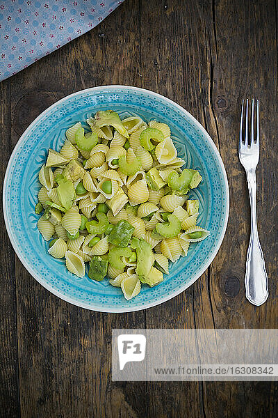 Teller Nudelsalat mit Avocado  Erbsen und Staudensellerie auf Holz  Ansicht von oben