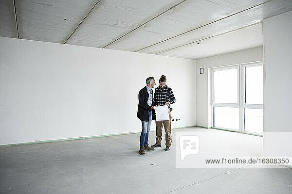 Architekt und Bauarbeiter besprechen einen Bauplan  während sie in einem leeren Haus stehen
