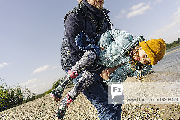 Father carrying daughter while enjoying near river bank