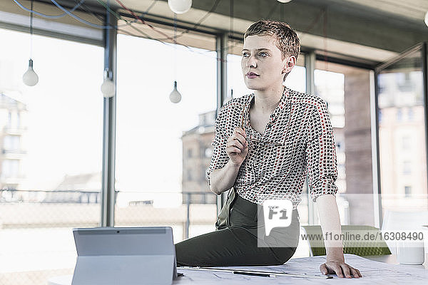 Nachdenkliche Geschäftsfrau auf dem Schreibtisch im Büro sitzend