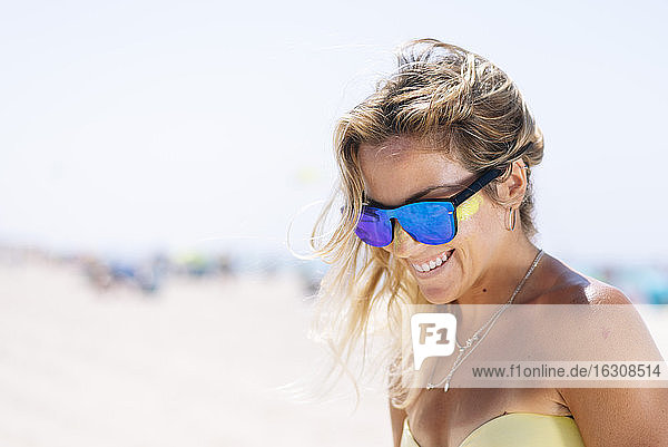 Happy young woman looking down while standing against beach