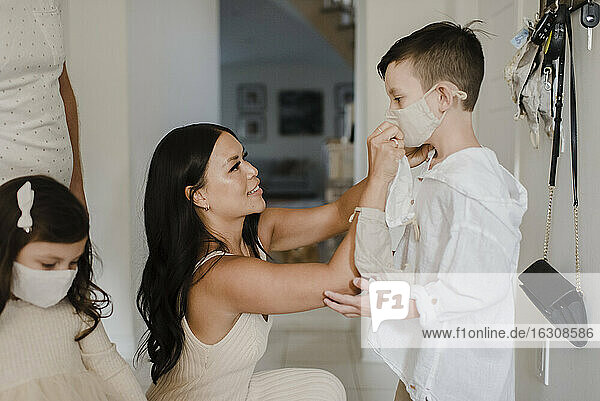 Mutter bedeckt das Gesicht ihres Sohnes mit einer Schutzmaske zu Hause während COVID-19