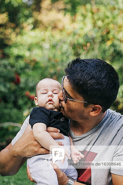 Young man kissing cute son at park during weekend